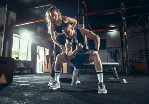 Athletic man and woman with a dumbbells training and practicing in gym. Concept of sport, healthy lifestyle, wellbeing.